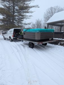LR Moving and Delivery safely transporting a covered hot tub on a flatbed trailer during a winter move at a residential property in Ontario.