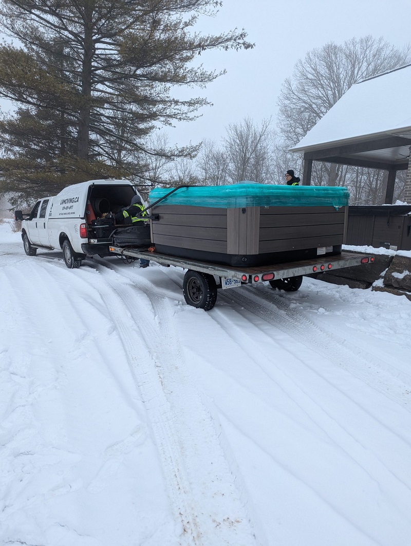 LR Moving and Delivery safely transporting a covered hot tub on a flatbed trailer during a winter move at a residential property in Ontario.